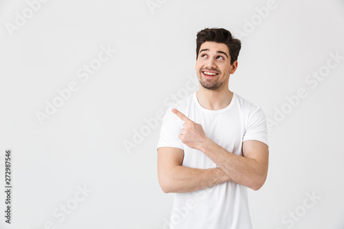 Excited young man posing isolated over white wall background pointing.