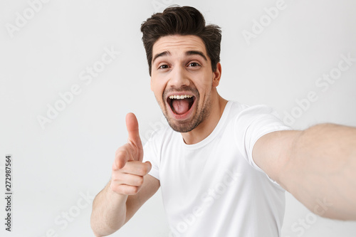 Excited happy young man posing isolated over white wall background make a selfie by camera.