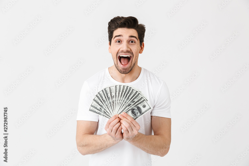 Shocked excited happy young man posing isolated over white wall background holding money. Shocked excited happy young man posing isolated over white wall background holding money.