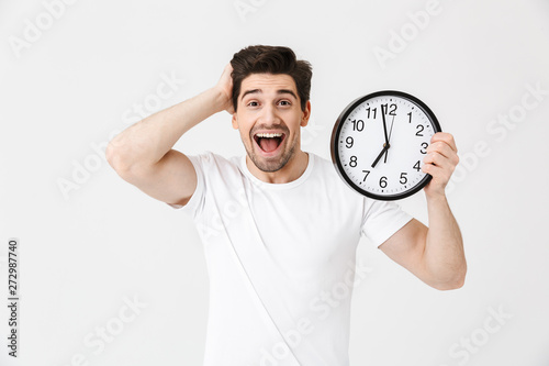 Shocked excited happy young man posing isolated over white wall background holding clock.