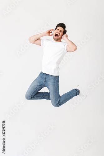 Emotional excited young man posing isolated over white wall background listening music with headphones.