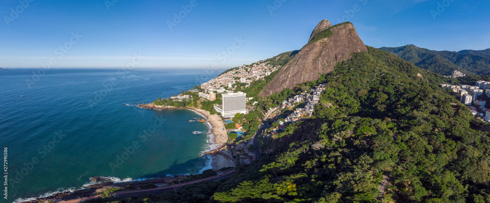 Aerial panorama of Rio de Janeiro Two Brothers mountain and peaks and coastal side against a blue sky with clouds. Natural landscape with urban shantytown community among natural coastal surrounding.
