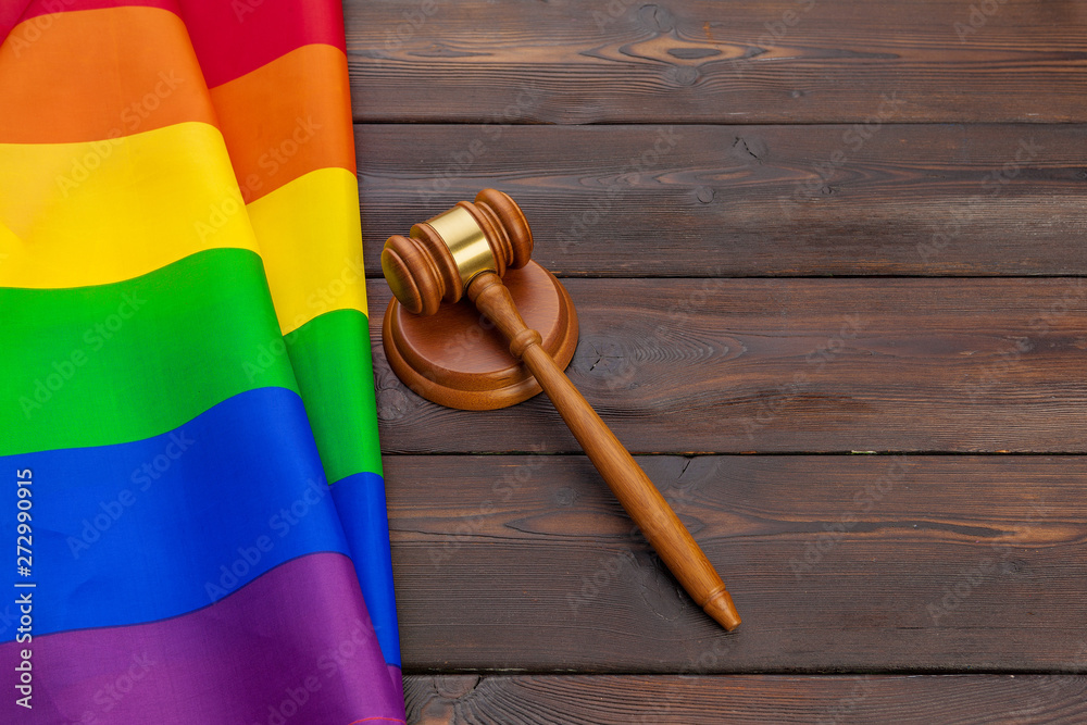 Woden judge mallet symbol of law and justice with lgbt flag in rainbow colours on wooden background