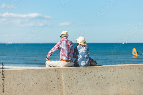 Loving the elderly couple sitting on the wall facing the beach, watching and taking pictures of the landscape on a romantic trip