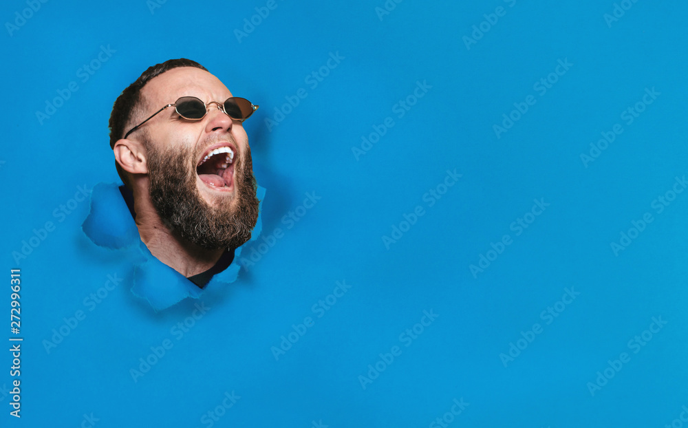 Screaming male face through hole in blue paper. Poin to your text. Discount, sale, season. space for your inscription. - obrazy, fototapety, plakaty 