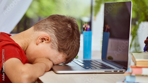 he rested his forehead in the computer symbolizing the helplessness in the face of difficulties.little boy student sitting at table with books, depression no desire to learn