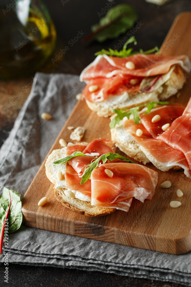 Traditional parma cured ham antipasto. Bruschetta set with Parma Ham and Parmesan Cheese. Small sandwiches with prosciutto, parmesan cheese, fresh arugula, olives and pine nuts Traditional parma cured ham antipasto. Bruschetta set with Parma Ham and Parmesan Cheese. Small sandwiches with prosciutto, parmesan cheese, fresh arugula, olives and pine nuts