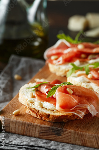 Traditional parma cured ham antipasto. Bruschetta set with Parma Ham and Parmesan Cheese. Small sandwiches with prosciutto, parmesan cheese, fresh arugula, olives and pine nuts