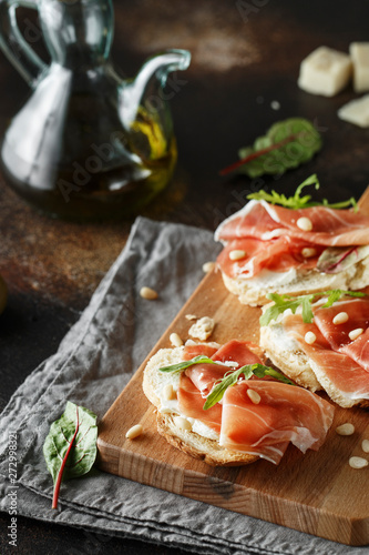 Traditional parma cured ham antipasto. Bruschetta set with Parma Ham and Parmesan Cheese. Small sandwiches with prosciutto  parmesan cheese  fresh arugula  olives and pine nuts