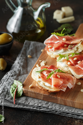 Traditional parma cured ham antipasto. Bruschetta set with Parma Ham and Parmesan Cheese. Small sandwiches with prosciutto, parmesan cheese, fresh arugula, olives and pine nuts