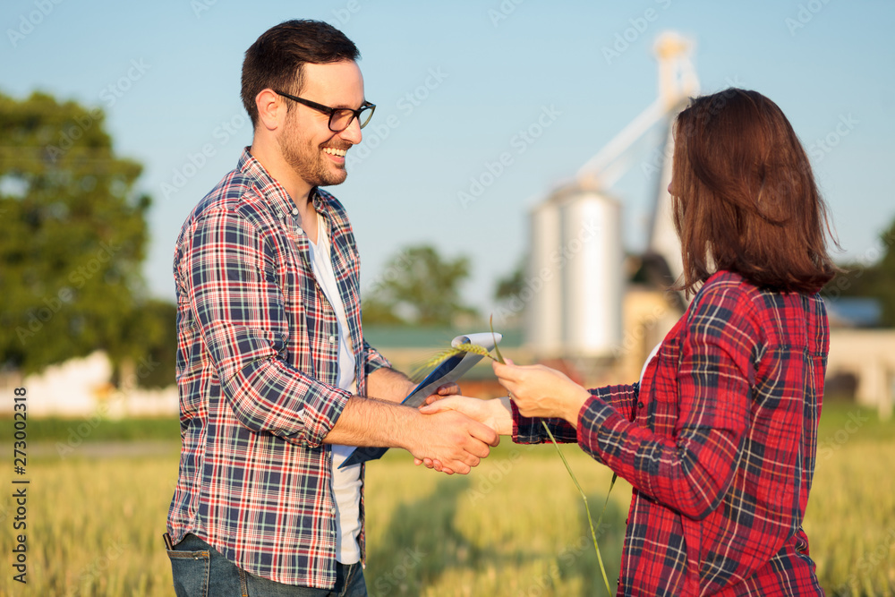 Two happy young female and male farmers or agronomists shaking hands after inspection of a wheat field. Organic farming and healthy food production