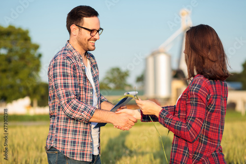 Obraz na płótnie Two happy young female and male farmers or agronomists shaking hands after inspection of a wheat field. Organic farming and healthy food production w salonie