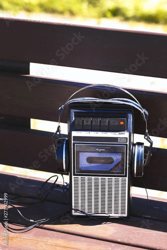 Retro vintage old 80s , 90s style portable radio audio cassette recorder player with audio tape cassette inside  with retro headphones on bench