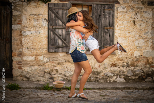 Mother and her daughter are enjoying at in front of the rustic stone wall . Embracing, jumping and hugging .