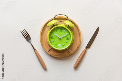 Diet and weight loss for healthy intermittent fasting lunchtime . Alarm clock and plate with cutlery on concrete background. Diet and Healthy Concept