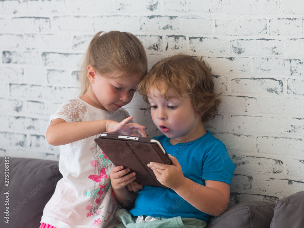 Brother and sister play games on the tablet, watch cartoons and laugh