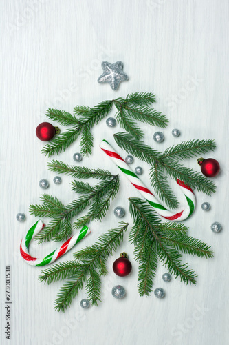 Christmas tree concept with green fir tree branches, glitter globules, red baubles and candy canes on white background