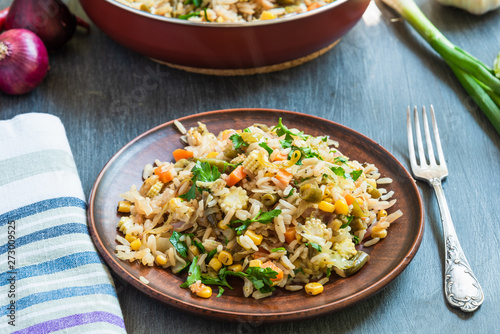Veggie fried rice with cabbage, carrots, corn, onion, beans and pepper with chopped parsley and chili in a plate on a wooden table, fork and napkin rustic style - Indian and Asian cuisine