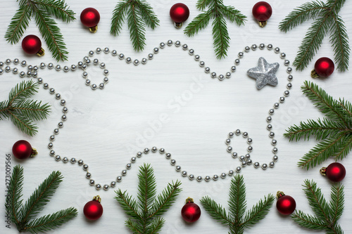 Christmas card concept with fir tree branches, red baubles, one brocade star and silver bead chain on white wooden background - text space