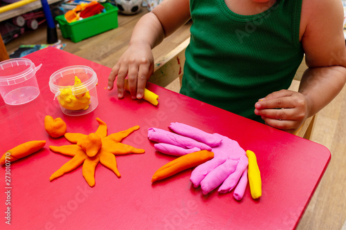 improving fine motor skills educational games concept, modeling soft clay plasticine children's hands close-up red background