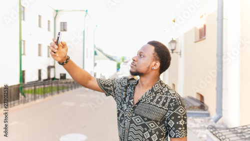 African cheerful crazy  man holding camera in hands and make a selfie outdoors.