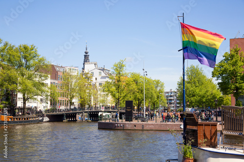 Gay pride peace rainbow flag and Amsterdam canal houses background.
