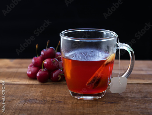 Un té rojo en una taza transparente de cristal junto a un puñado de cerezas rojas 