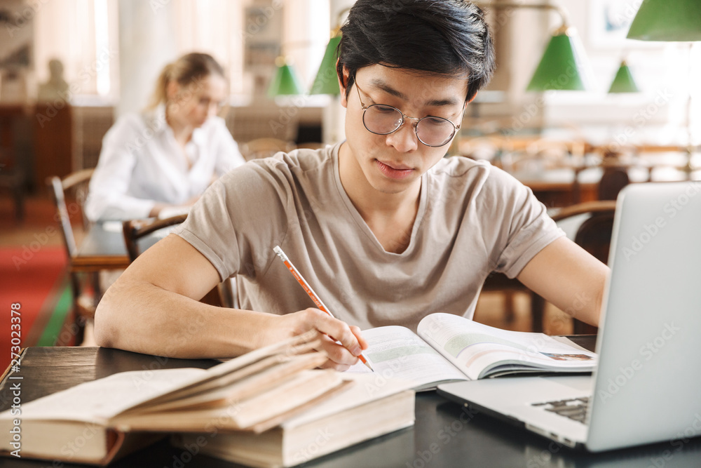 Smart cheerful teenagers studying at the library together Smart cheerful teenagers studying at the library together