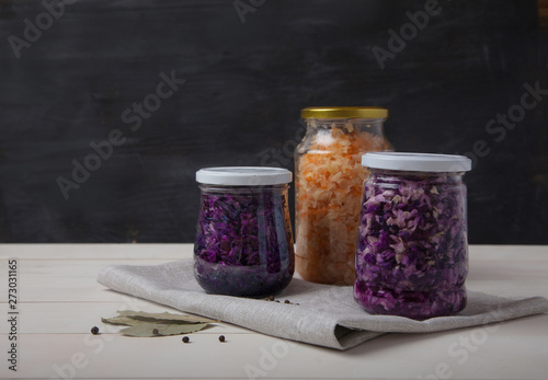 fermented white and red cabbage in glass jars on a white wooden table on a black background
