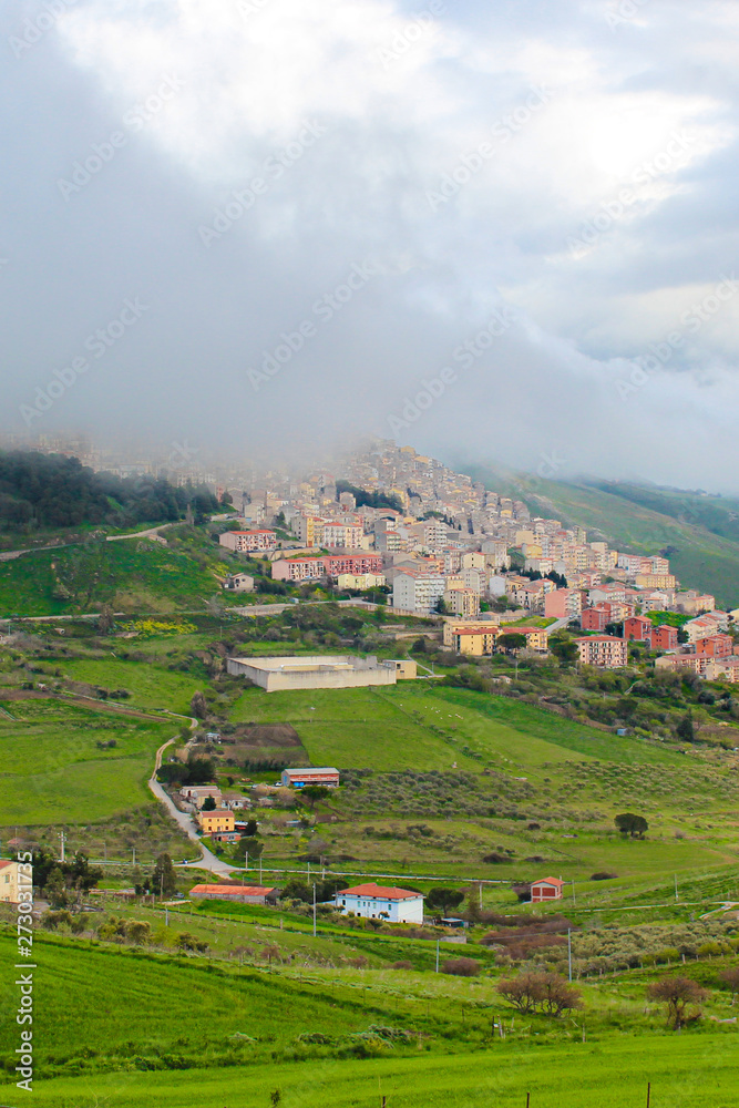 Vertical photo of picturesque Sicilian village Gangi in Italy captured in fog. The small historical city is surrounded by green landscape and is located on the top of the hills. Italian countryside