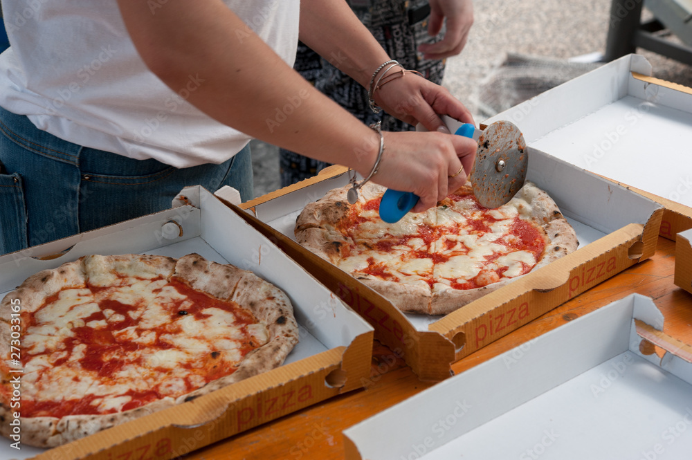 Hot pizza Margherita cut into slices, ready to take-away in cardboard boxes.
