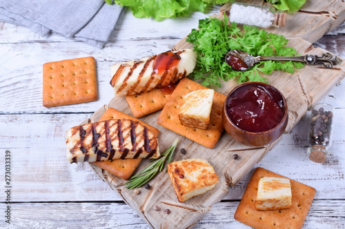 Grilled adyghe cheese, crackers, red jam, spices and cress salad on the wooden board against the white background