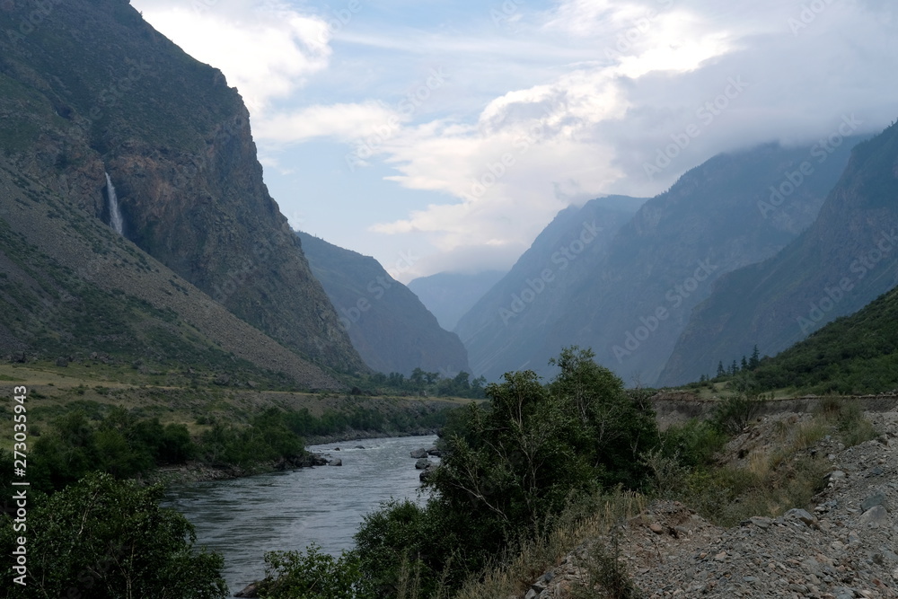 Evening landscape of mountain slopes between which a small river flows.