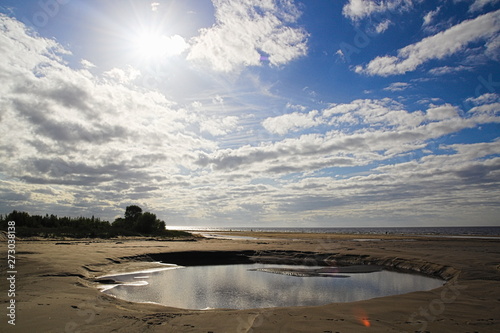 A medium sized water puddle beach sand sea clouds sunny