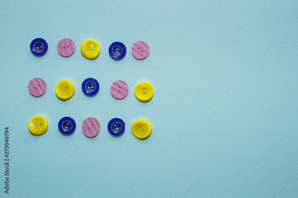 collection of various multicolored sewing button on blue background. Yellow, purple, dark blue buttons. Minimalism. Sewing accessories. Flatlay, place for text