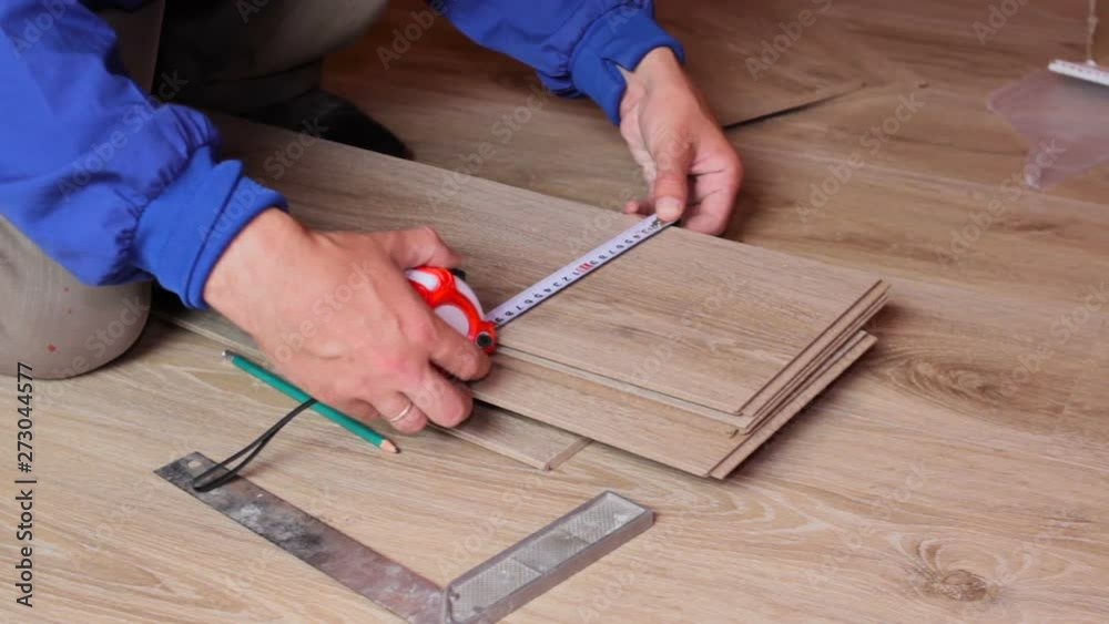 man measures the board metal tape measure,measure the laminate board in the room, work on the installation of laminate flooring man measures the board metal tape measure,measure the laminate board in the room, work on the installation of laminate flooring