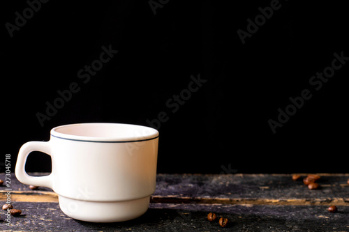 White coffee mug on wooden table and black background with space for text. Composition for coffee shop and coffee making