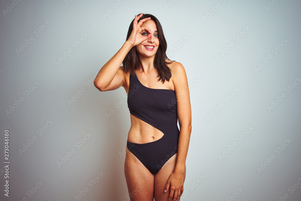 Beautiful woman wearing bikini swimwear over white isolated background doing ok gesture with hand smiling, eye looking through fingers with happy face.