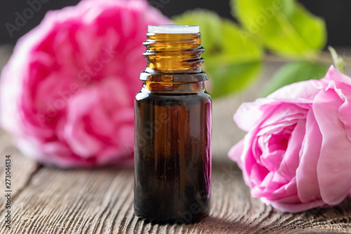 A bottle of rose essential oil with rose flowers