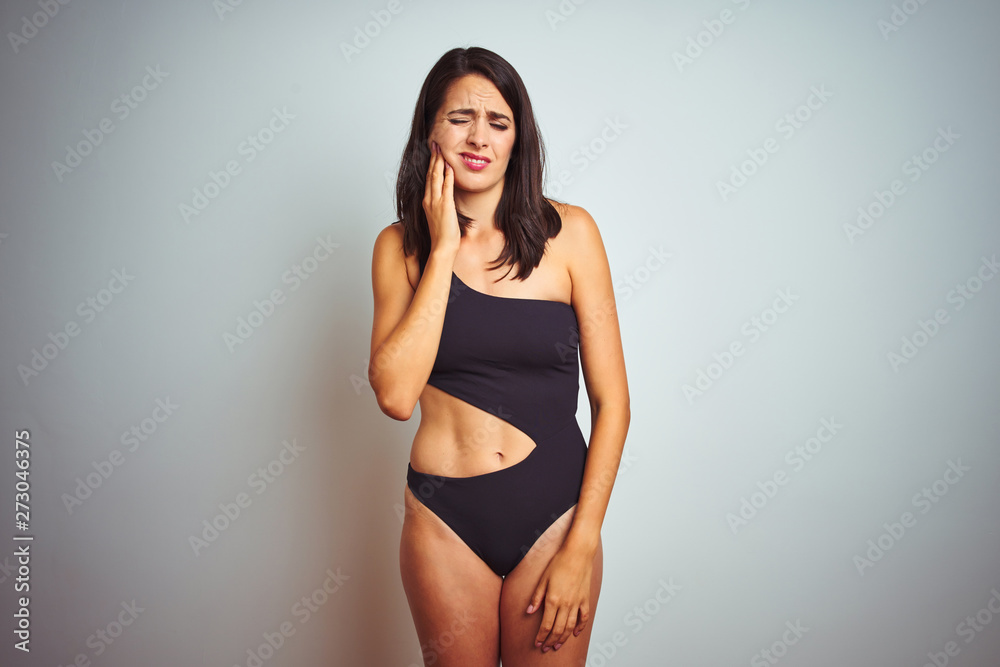 Beautiful woman wearing bikini swimwear over white isolated background touching mouth with hand with painful expression because of toothache or dental illness on teeth. Dentist concept. Beautiful woman wearing bikini swimwear over white isolated background touching mouth with hand with painful expression because of toothache or dental illness on teeth. Dentist concept.