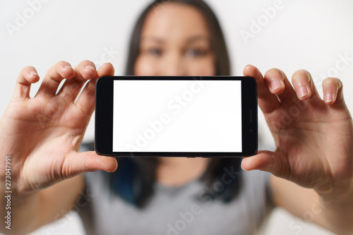 A nice woman holding a smartphone with an empty white screen with two hands horizontally and smiling On white background