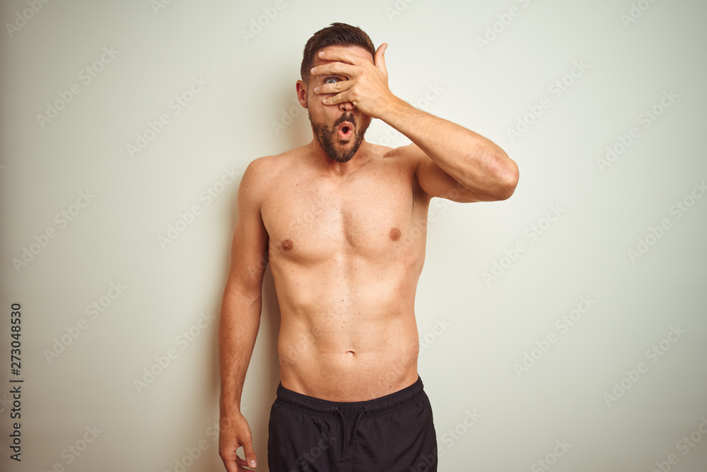 Fototapeta premium Young handsome shirtless man over isolated background peeking in shock covering face and eyes with hand, looking through fingers with embarrassed expression.
