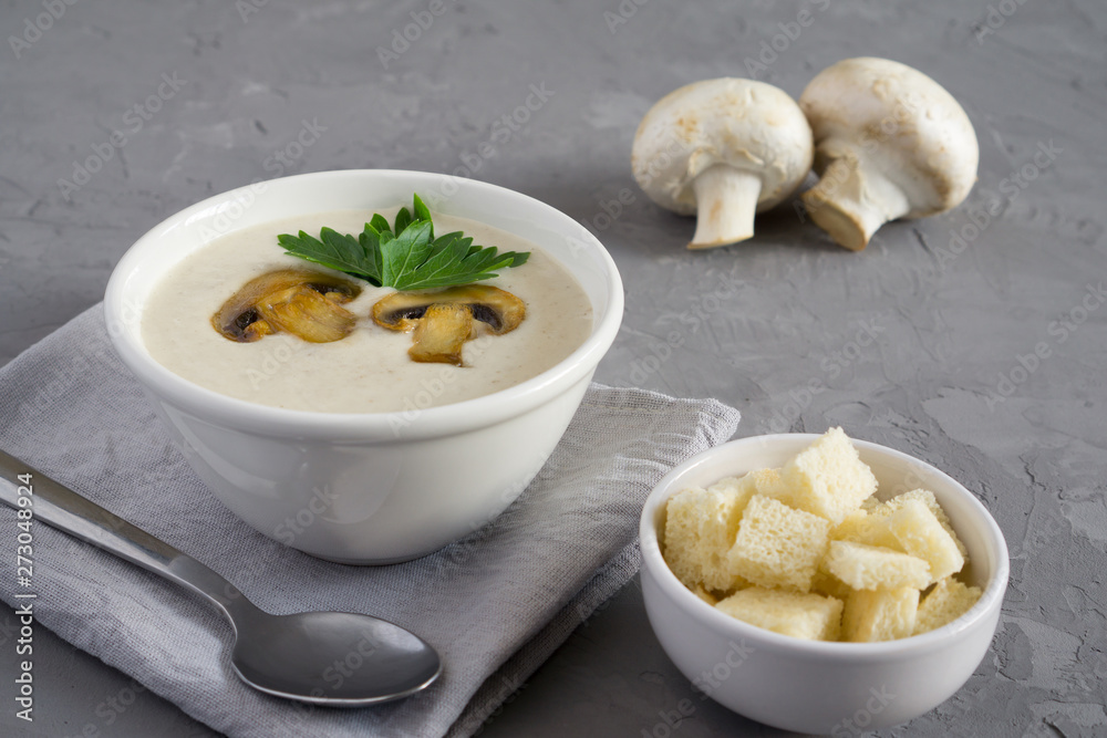 Champignon mushroom cream soup in a white bowl with parsley and crackers on a concrete gray background with copy space Champignon mushroom cream soup in a white bowl with parsley and crackers on a concrete gray background with copy space