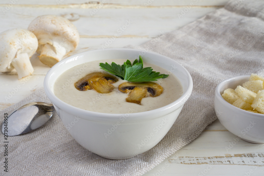Champignon mushroom cream soup in a white bowl with parsley and crackers on a white wooden background with copy space Champignon mushroom cream soup in a white bowl with parsley and crackers on a white wooden background with copy space