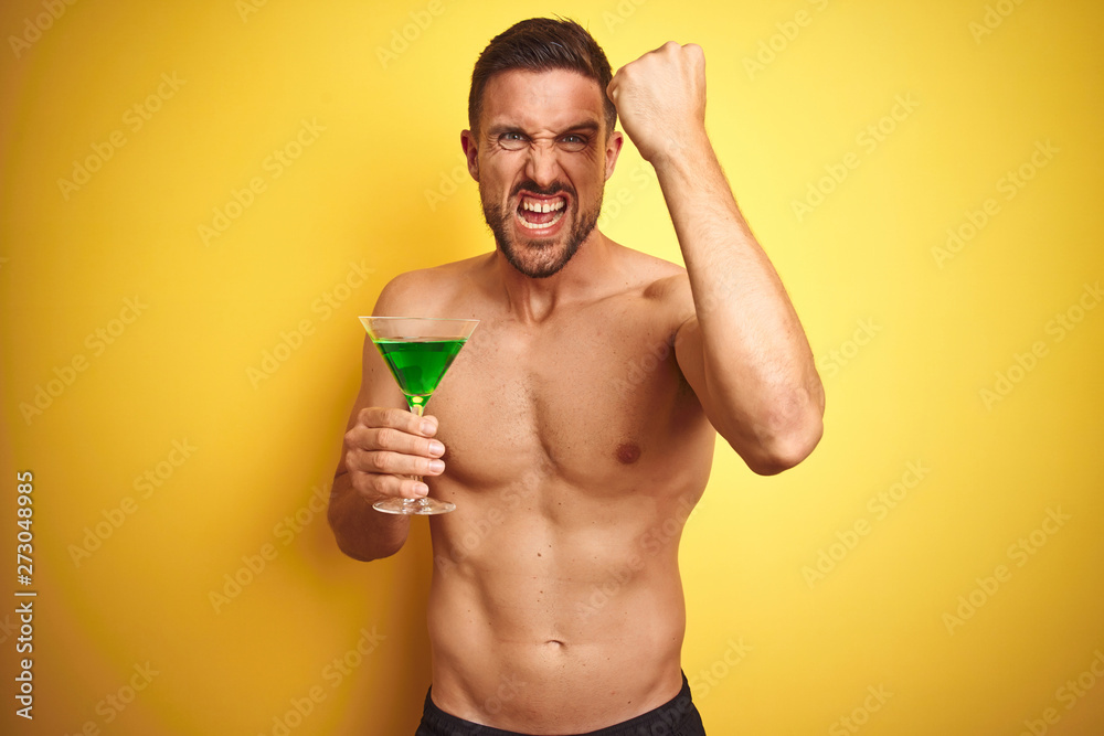 Young handsome shirtless man drinking a summer cocktail over isolated yellow background annoyed and frustrated shouting with anger, crazy and yelling with raised hand, anger concept Young handsome shirtless man drinking a summer cocktail over isolated yellow background annoyed and frustrated shouting with anger, crazy and yelling with raised hand, anger concept