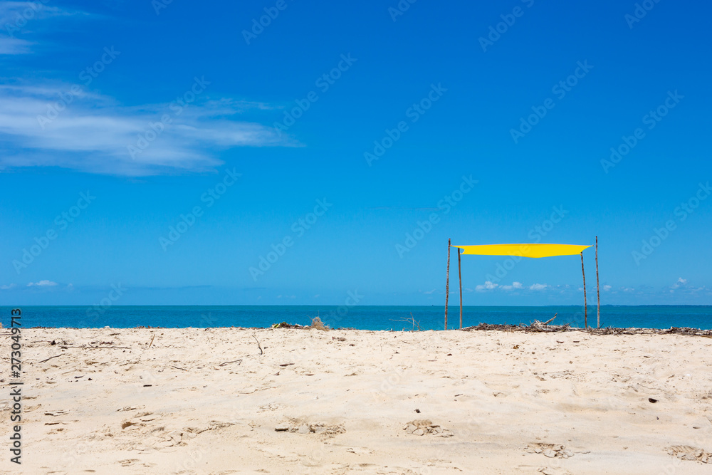 Beautiful beach view with a yellow tent on sunny summer day and sea and blue sky in the background. Concept of vacations, peace and relaxation. Ponta do Corumbau, Bahia, Brazil. Beautiful beach view with a yellow tent on sunny summer day and sea and blue sky in the background. Concept of vacations, peace and relaxation. Ponta do Corumbau, Bahia, Brazil.