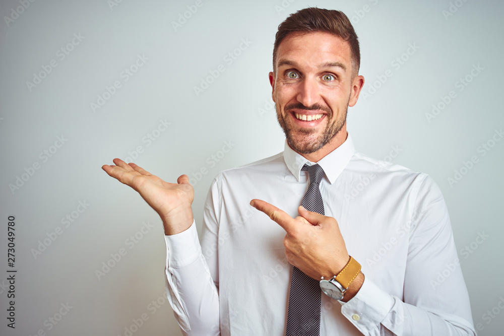 Young handsome business man wearing elegant white shirt over isolated background amazed and smiling to the camera while presenting with hand and pointing with finger. Young handsome business man wearing elegant white shirt over isolated background amazed and smiling to the camera while presenting with hand and pointing with finger.