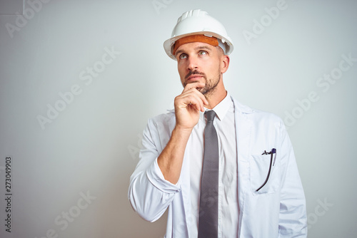 Young handsome engineer man wearing safety helmet over isolated background with hand on chin thinking about question, pensive expression. Smiling with thoughtful face. Doubt concept.