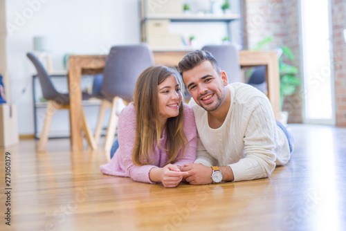 Young beautiful couple in love moving to new home, lying on the floor around cardboard boxes, very happy and cheerful for new apartment