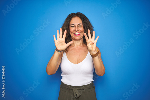 Middle age senior woman with curly hair standing over blue isolated background showing and pointing up with fingers number nine while smiling confident and happy.